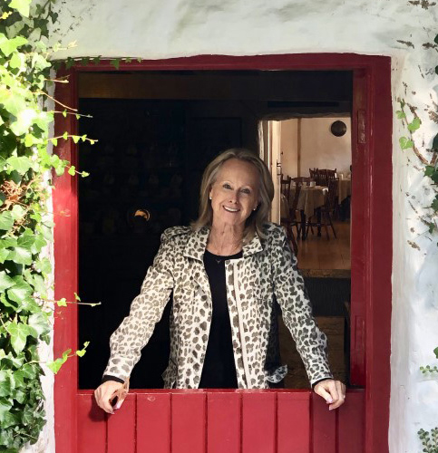 Marie-Claude Arnott smiles and welcomes her website visitors standing at a red door open at the top.